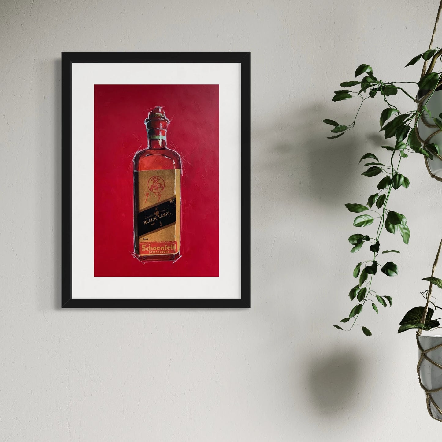 Gerahmter Kunstdruck einer Johnny Walker Flasche hängt an einer weissen Wand neben einer Zimmerpflanze