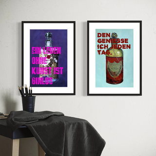 Zwei humorvolle Kunstdrucke mit Flaschenmotiven und auffälligen Sprüchen in kräftigen Farben hängen nebeneinander an einer weißen Wand über einem kleinen Tisch mit schwarzer Tischdecke und Stiftebecher. Der linke Druck zeigt eine Gin-Flasche mit dem Text „Ein Leben ohne Kunst ist ginlos“, der rechte eine Champagnerflasche mit dem Spruch „Den genieße ich jeden Tag“. Perfekt als originelle Wandbilder für die Wohnung oder als witzige Geschenke für Männer.