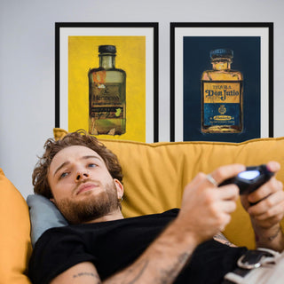 Junger Mann liegt auf einer gelben Couch und spielt mit seiner Spielekonsole. Im Hintergrund sind zwei Kunstdrucke an der Wand zu sehen.