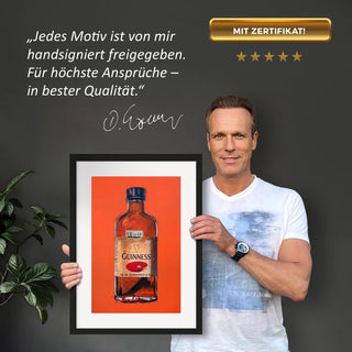 Dominik Lommer präsentiert den Kunstdruck Alkoholika Artefakt Guinness vor einer grauen Wand mit einem Zitat und Unterschrift