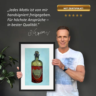 Dominik Lommer präsentiert den Kunstdruck Alkoholika Artefakt Dom Perignon vor einer grauen Wand mit einem Zitat und Unterschrift