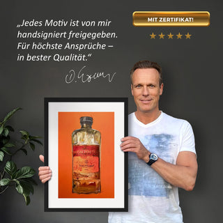 Dominik Lommer präsentiert den Kunstdruck Alkoholika Artefakt Veuve Clicquot vor einer grauen Wand mit einem Zitat und Unterschrift
