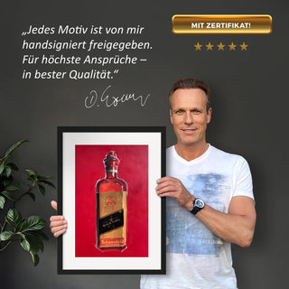 Dominik Lommer präsentiert den Kunstdruck Alkoholika Artefakt Johnny Walker vor einer grauen Wand mit einem Zitat und Unterschrift