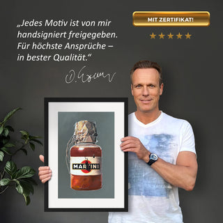 Dominik Lommer präsentiert den Kunstdruck Alkoholika Artefakt Martini vor einer grauen Wand mit einem Zitat und Unterschrift