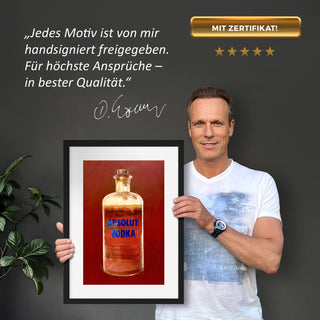 Dominik Lommer präsentiert den Kunstdruck Alkoholika Artefakt Absolut Vodka vor einer grauen Wand mit einem Zitat und Unterschrift