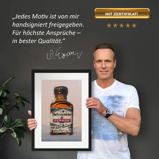 Dominik Lommer präsentiert den Kunstdruck Alkoholika Artefakt Pernod vor einer grauen Wand mit einem Zitat und Unterschrift