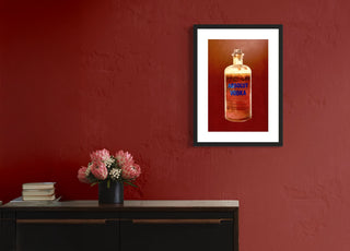 Kunstdruck Absolut Vodka inklusive Bilderrahmen hängt an einer roten Wand über einem Sideboard