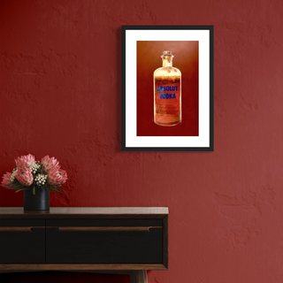 Kunstdruck Absolut Vodka inklusive Bilderrahmen hängt an einer roten Wand über einem Sideboard